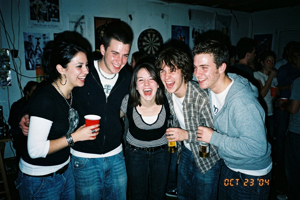 A candid flash photograph of a group of friends laughing at a party, shot in the style of a 2004 pocket digital camera with harsh direct flash and organic sensor noise.